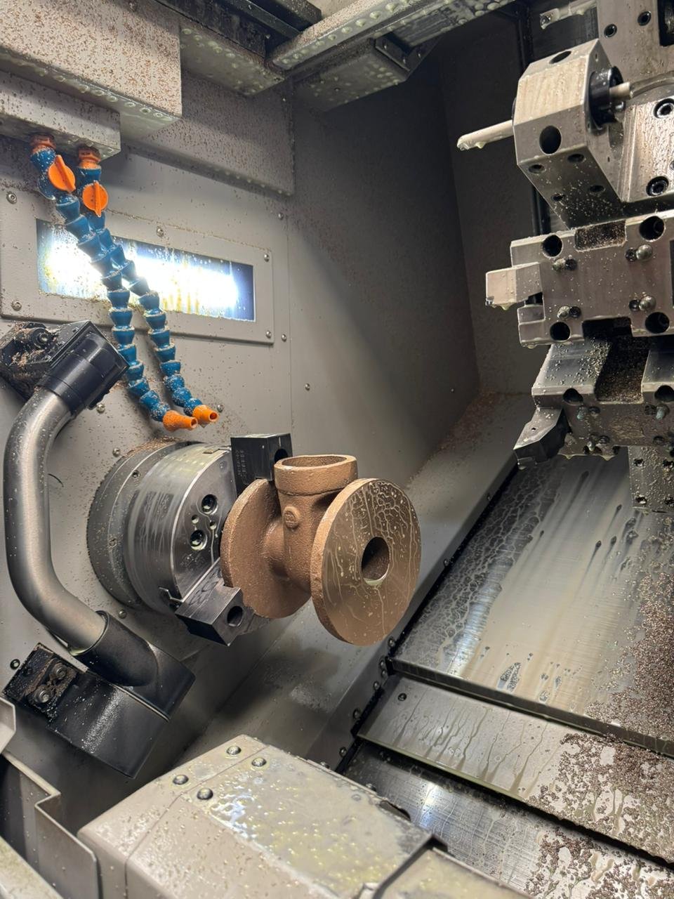 Válvula esférica de bronce siendo mecanizada en torno CNC con refrigerante